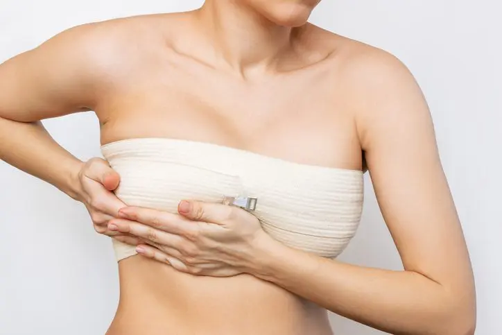 woman clutching the underside of her breast wrapped in a post-surgery bandage