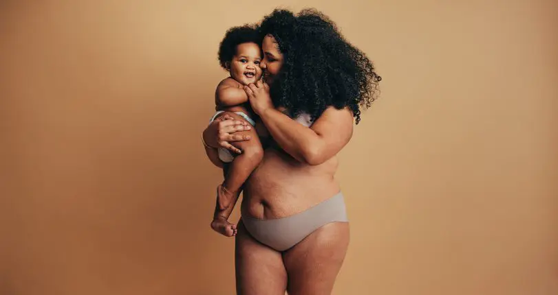 A mother holding her young child. She is happy and confident showing her post-pregnancy body. 