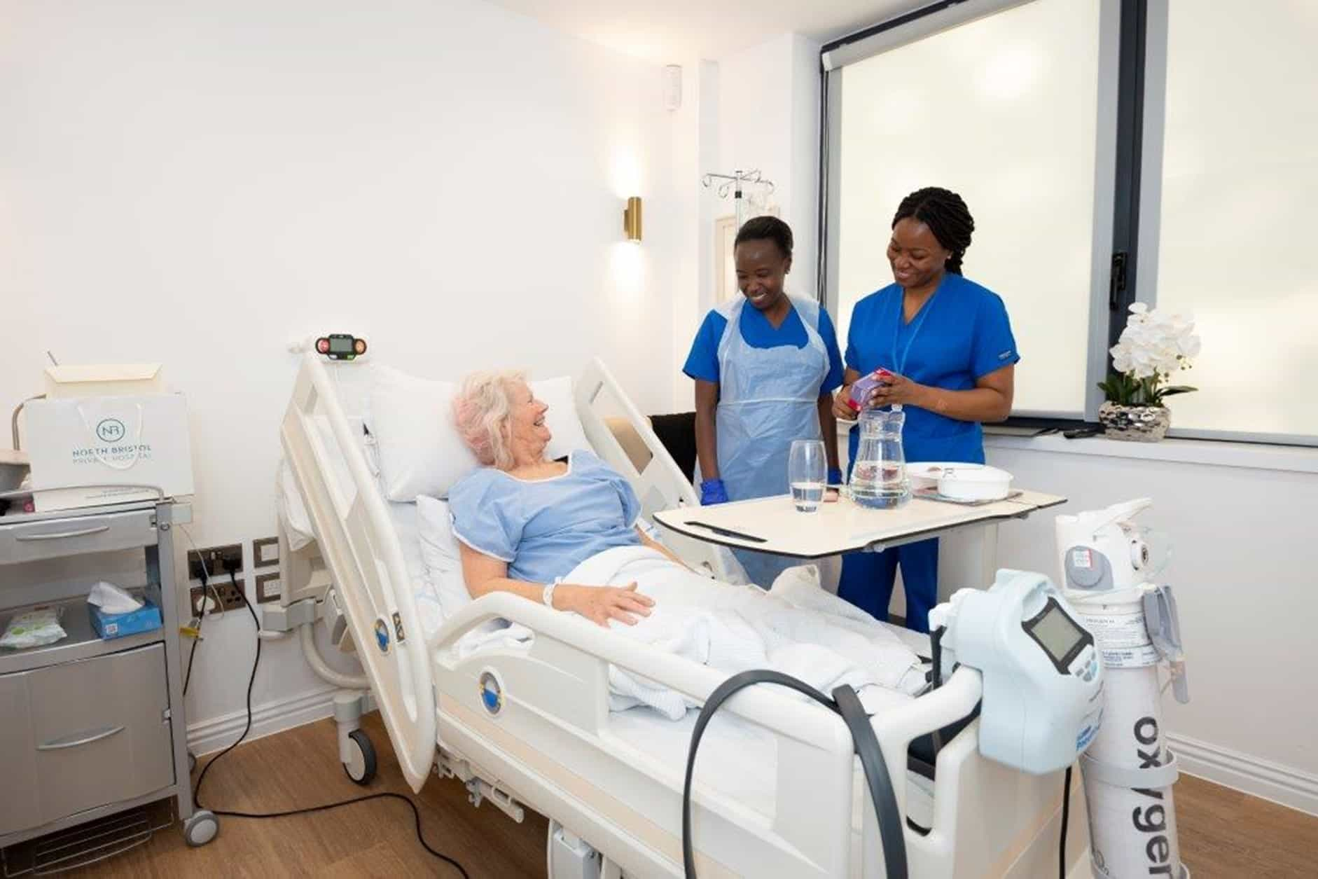 A woman lying in a hospital bed smiling up at two nurses at the bedside