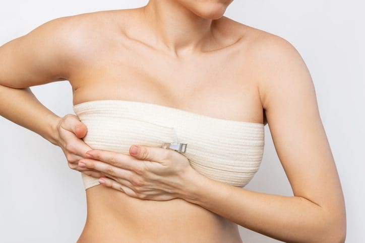 woman clutching the underside of her breast wrapped in a post-surgery bandage