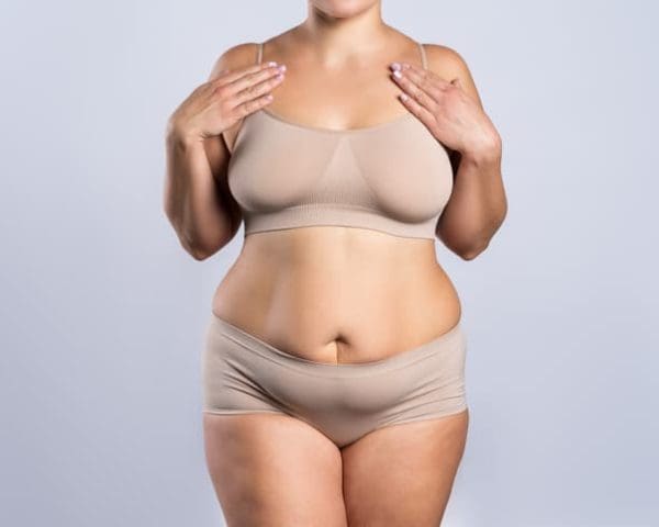 Woman in beige underwear on gray background, overweight female body