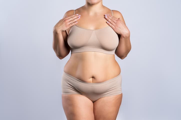  Woman in beige underwear on gray background, overweight female body